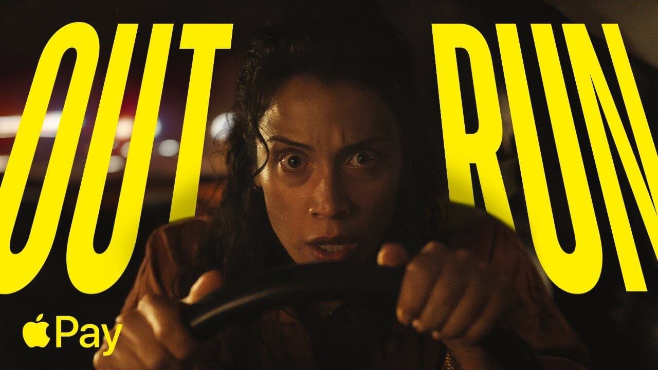 Mulher fugindo em carro com céu apocalíptico ao fundo, usando Apple Pay para pagar combustível